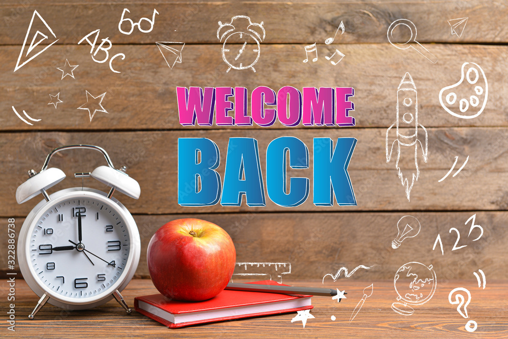 School supplies, apple, clock and text WELCOME BACK on wooden background