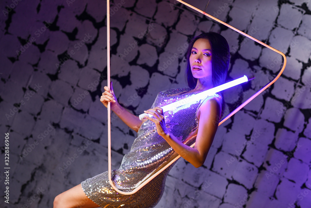 Toned portrait of young woman with neon lamps on dark color background