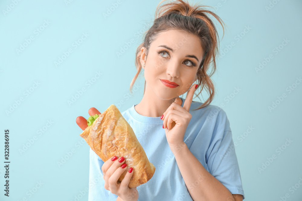 Portrait of thoughtful young woman with French hot dog on color background