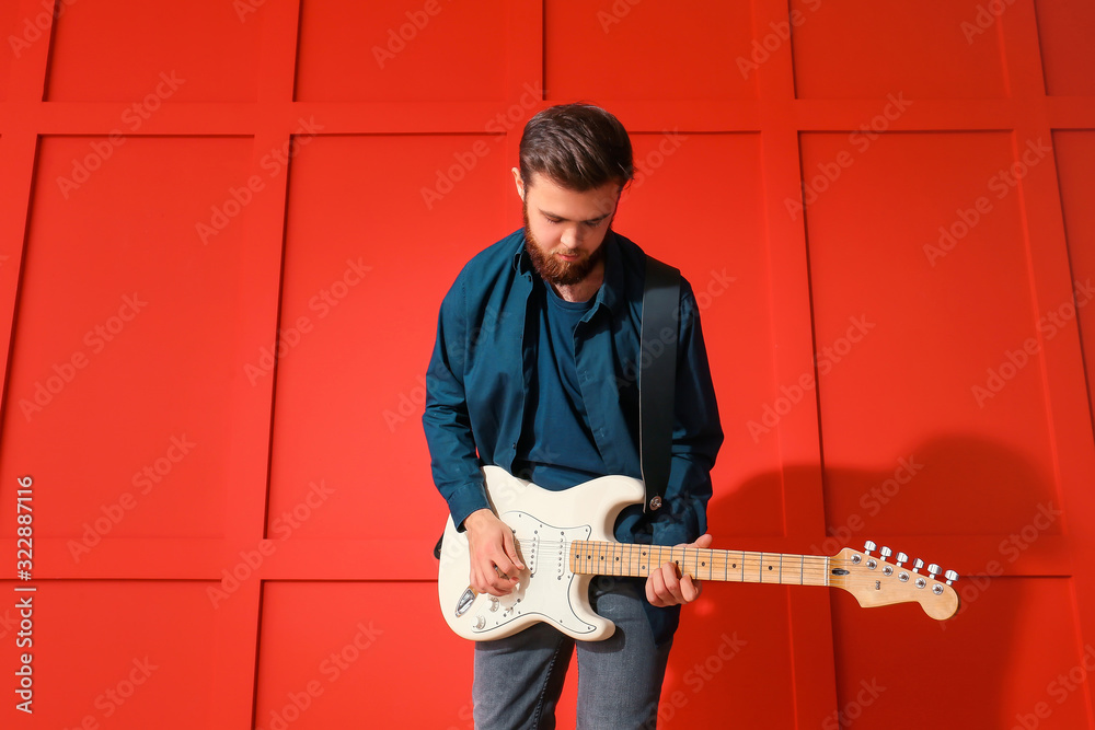 Young man playing guitar near color wall