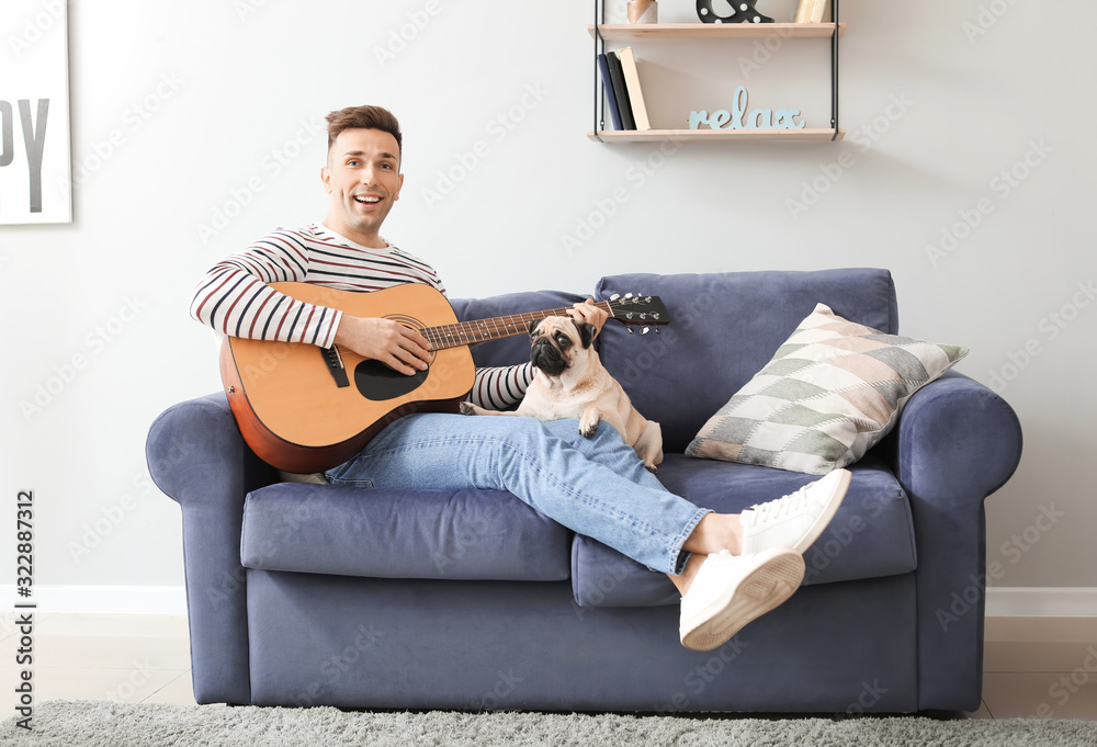 Handsome man with cute pug dog playing guitar at home