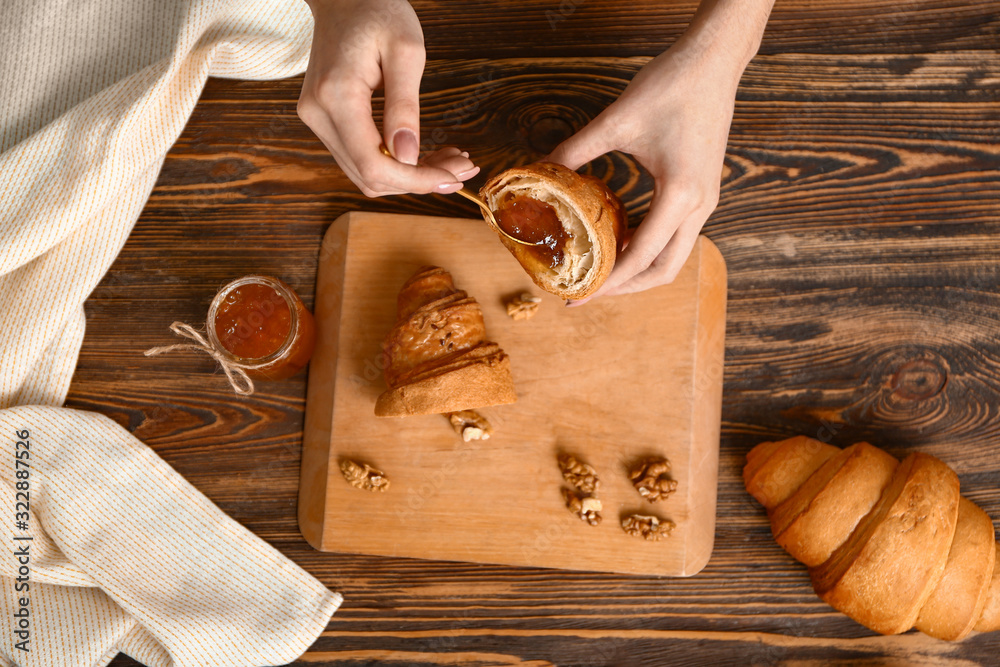 Woman filling croissant with jam, top view