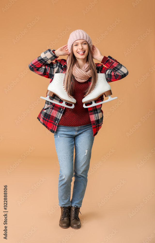 Beautiful young woman with ice skates on color background