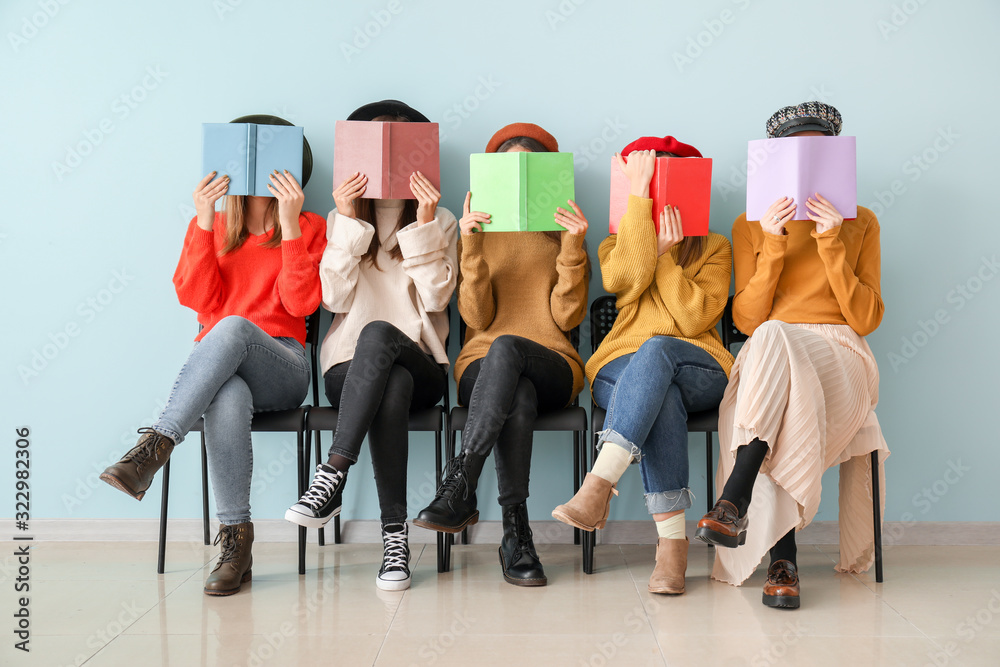 Young women with books sitting near color wall