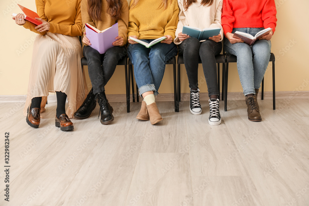 Young women with books sitting near color wall