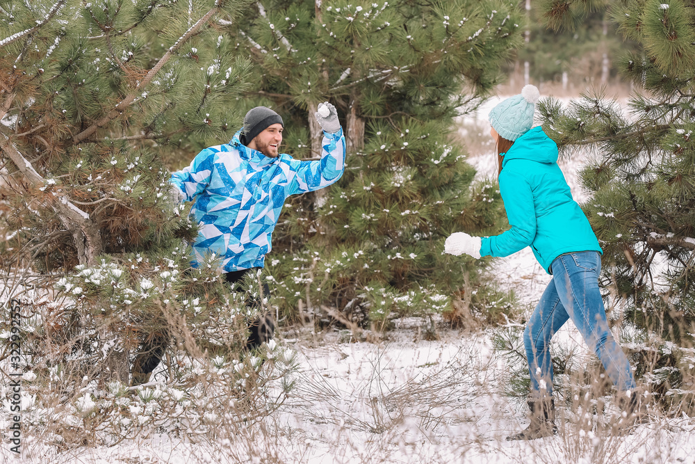 Happy young couple playing snowballs in park on winter day