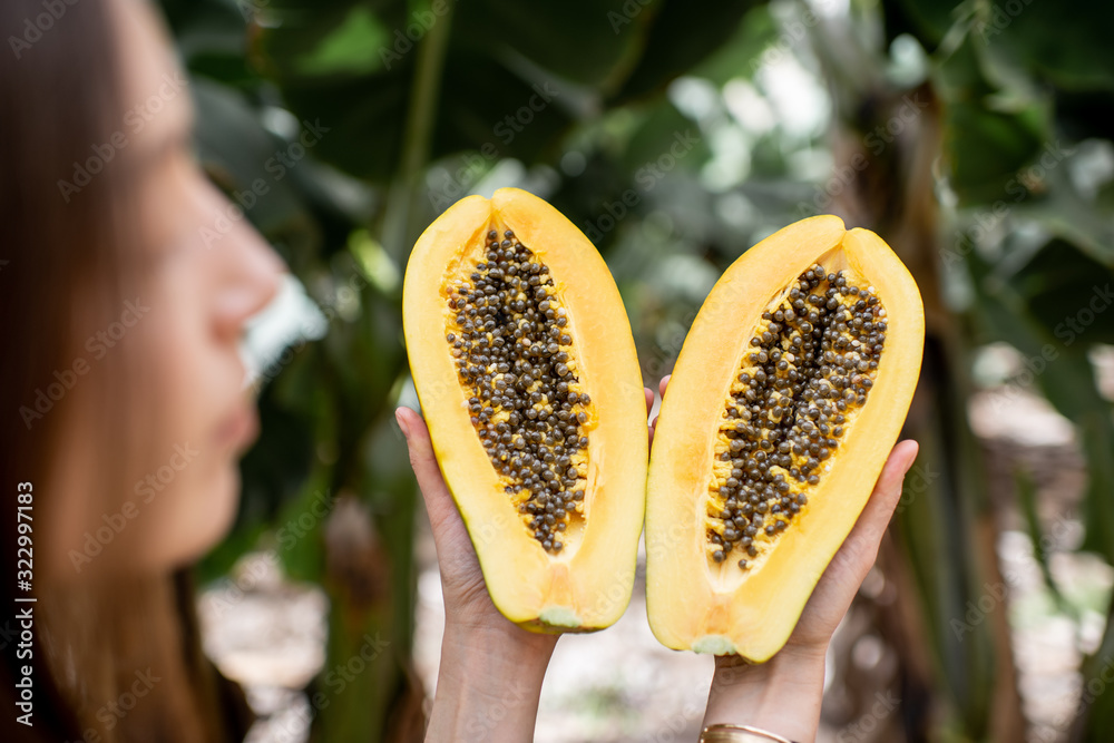 Portrait of a young woman with sliced papaya fruit on the plantation. Concept of vegetarianism, heal