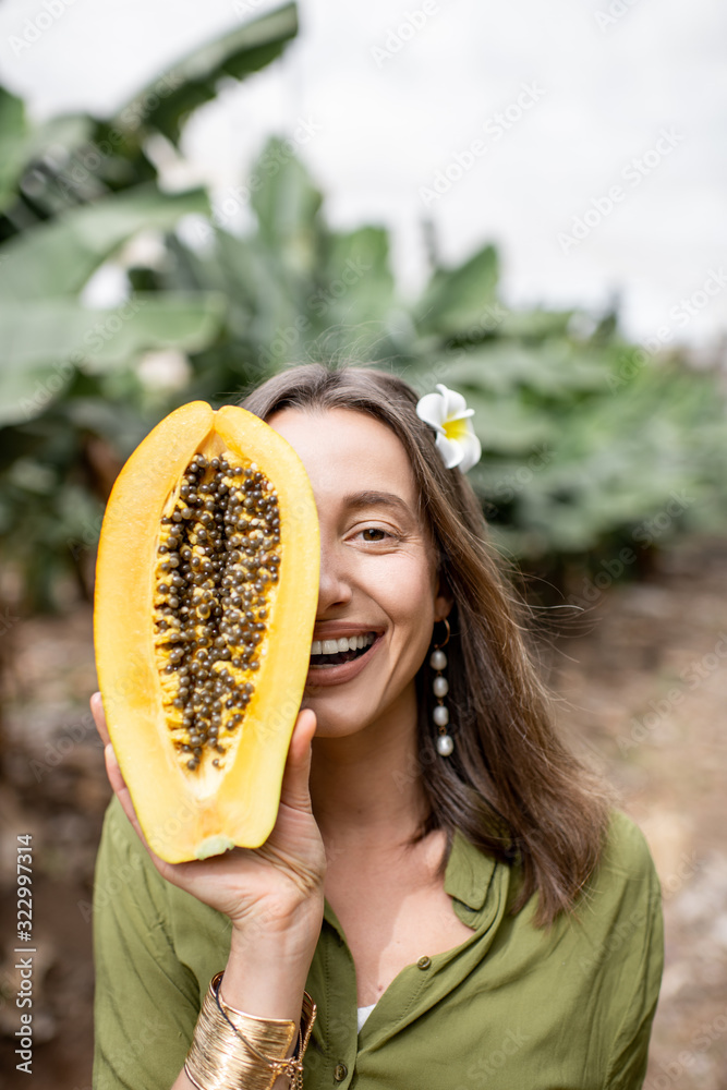 Closeup portrait of a young woman hiding her face behind sliced papaya fruit outdoors on the green b