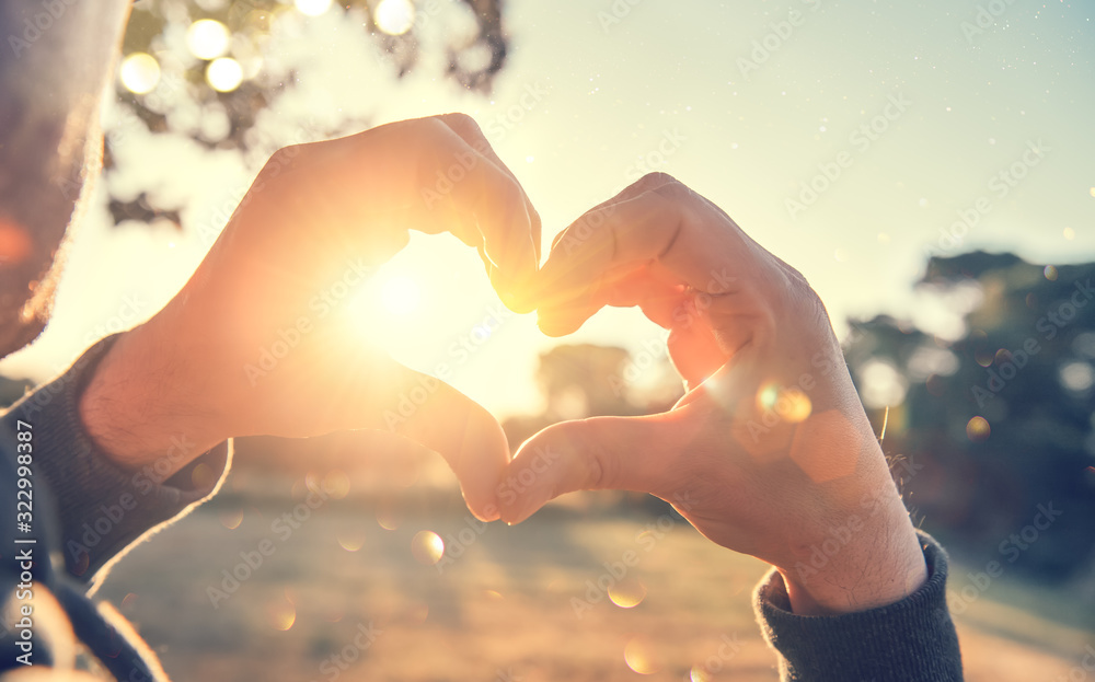 Person making heart with hands over nature sunset background. Happy young people. Silhouette hand in