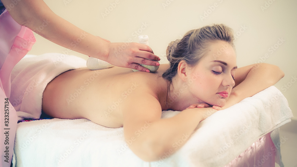 Massage therapist holds a herbal compress to do treatment to woman lying on spa bed in a luxury spa 