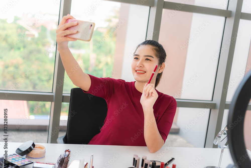 Young lady talking on cosmetics holding a makeup palette while recording her video. Woman making a v