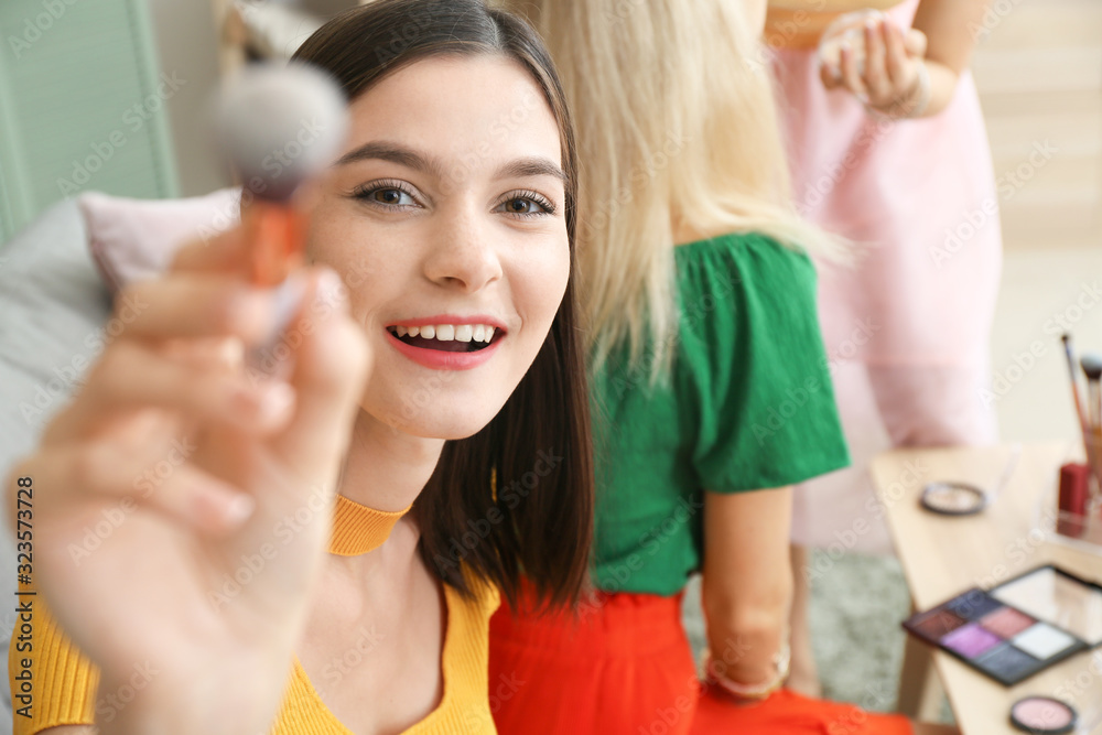 Beautiful young women applying makeup together at home