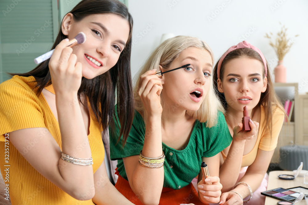 Beautiful young women applying makeup together at home