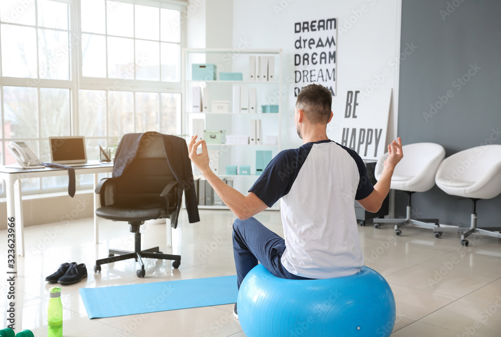 Man meditating on fitness ball in office