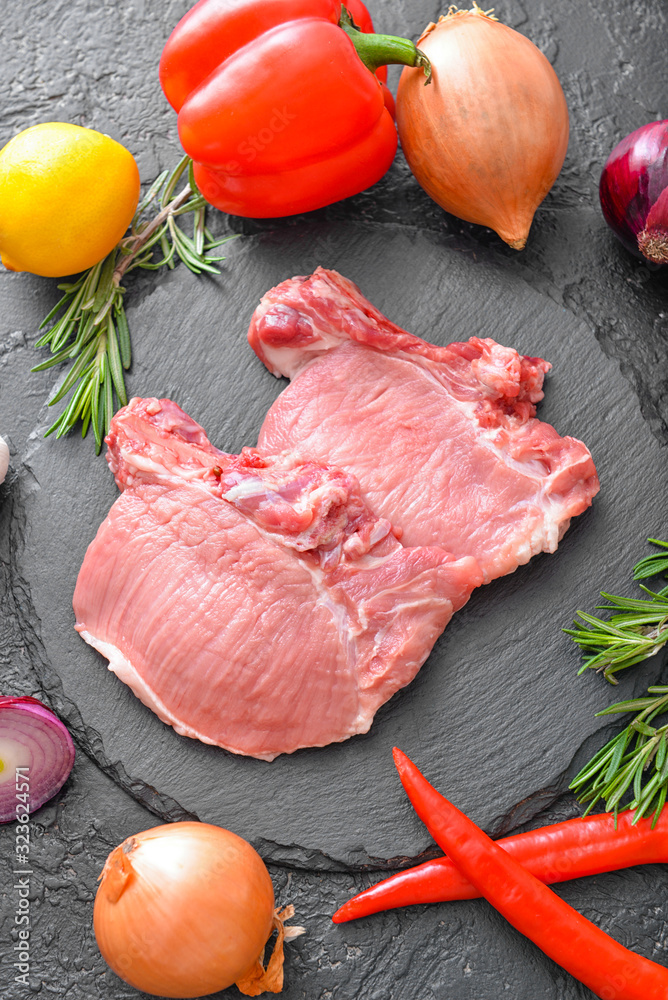 Raw pork meat with vegetables on dark background