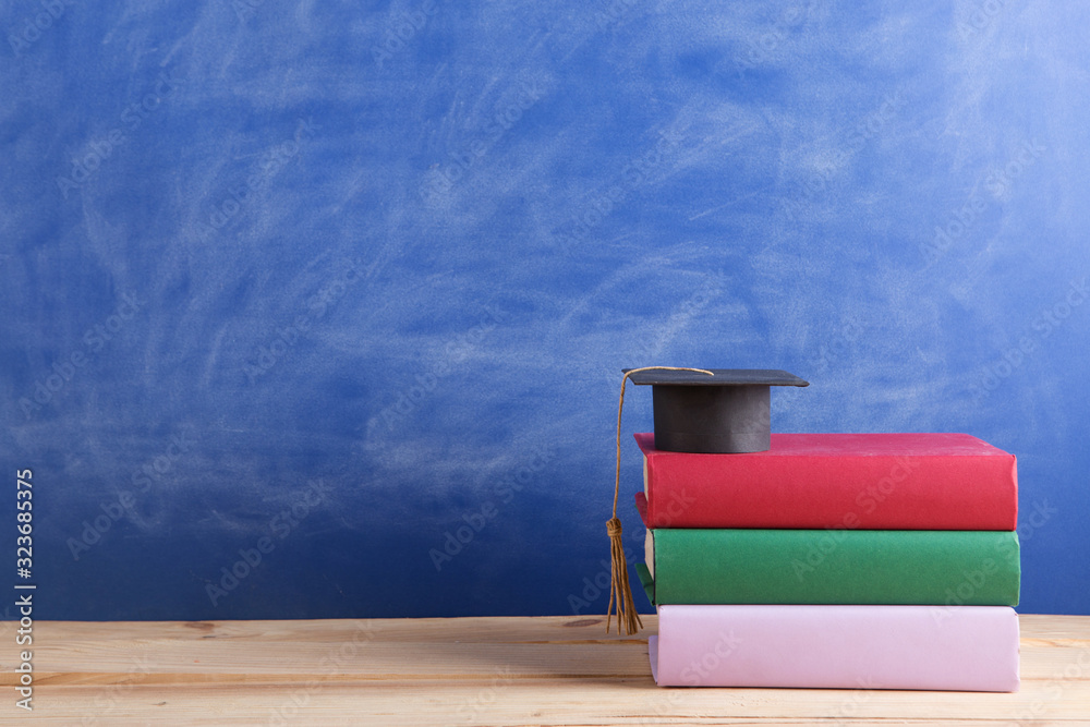 Graduation cap with books on the chalkboard background in the auditorium