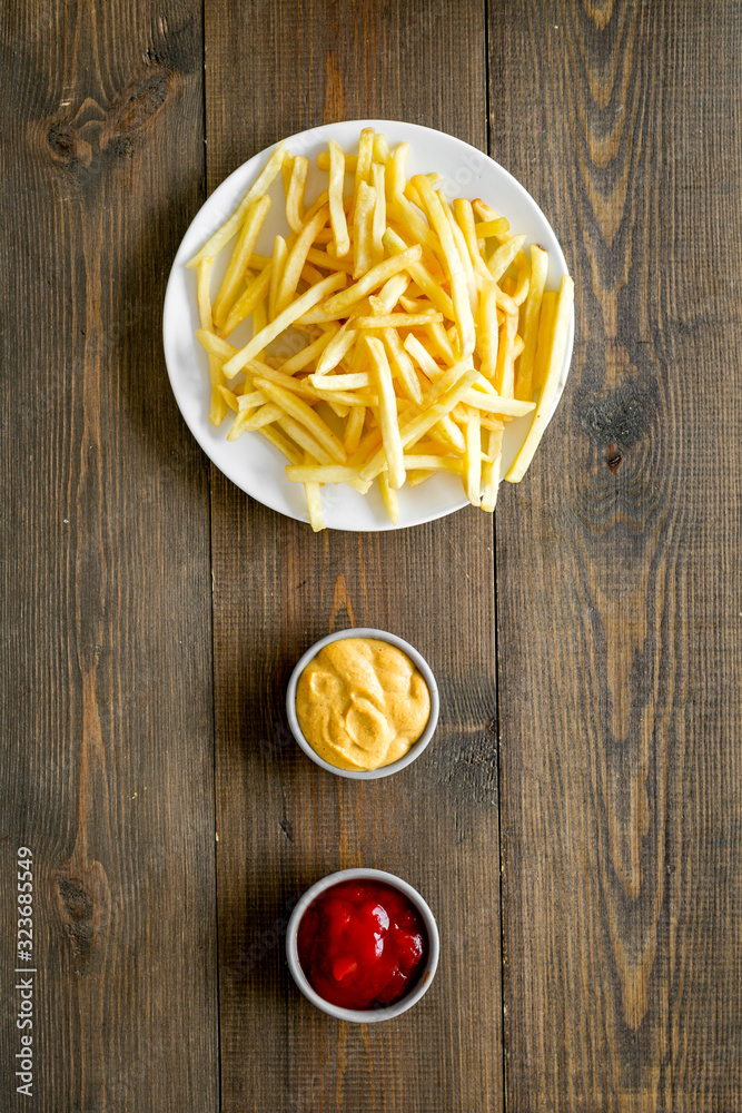 Fast food symbol. French fries on plate on dark wooden table top-down