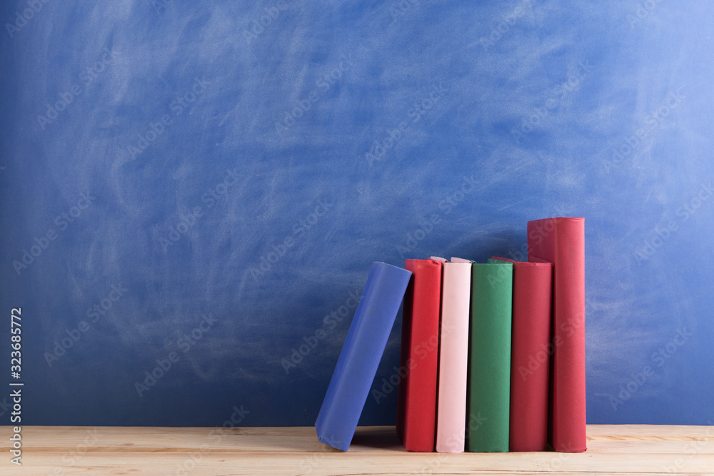 Education and reading concept - group of books on the wooden table, blue blackboard background. Teac