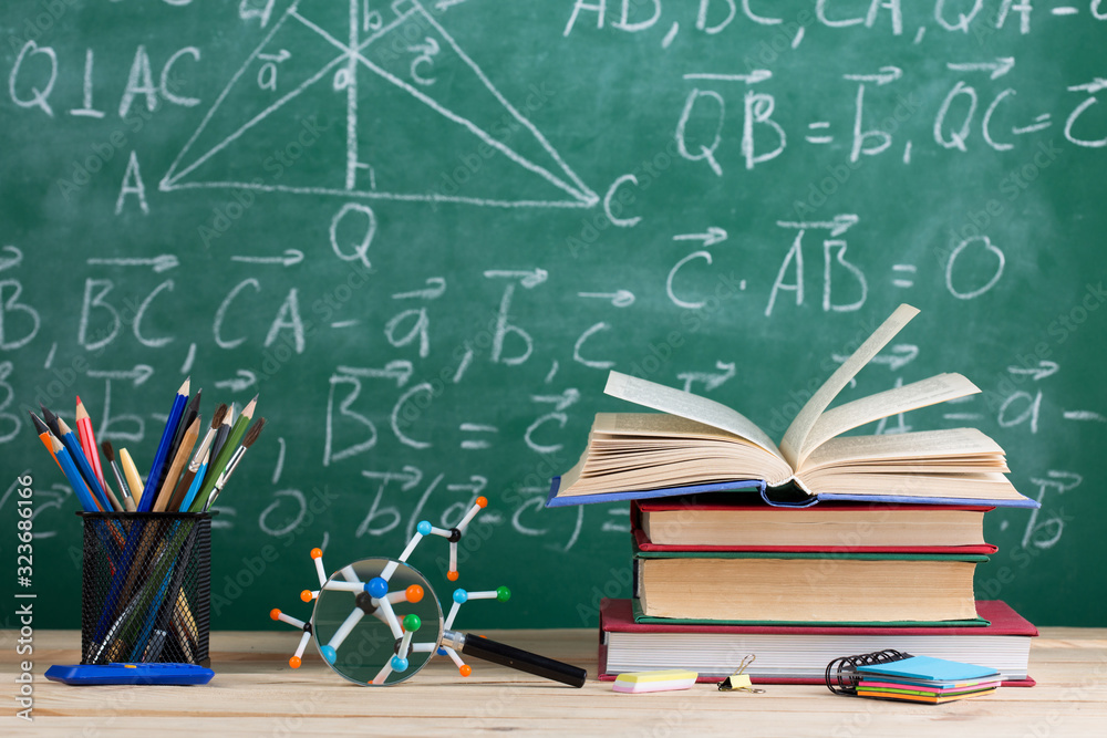 Education and sciences concept - books on the teacher desk in the auditorium, chalkboard on the back