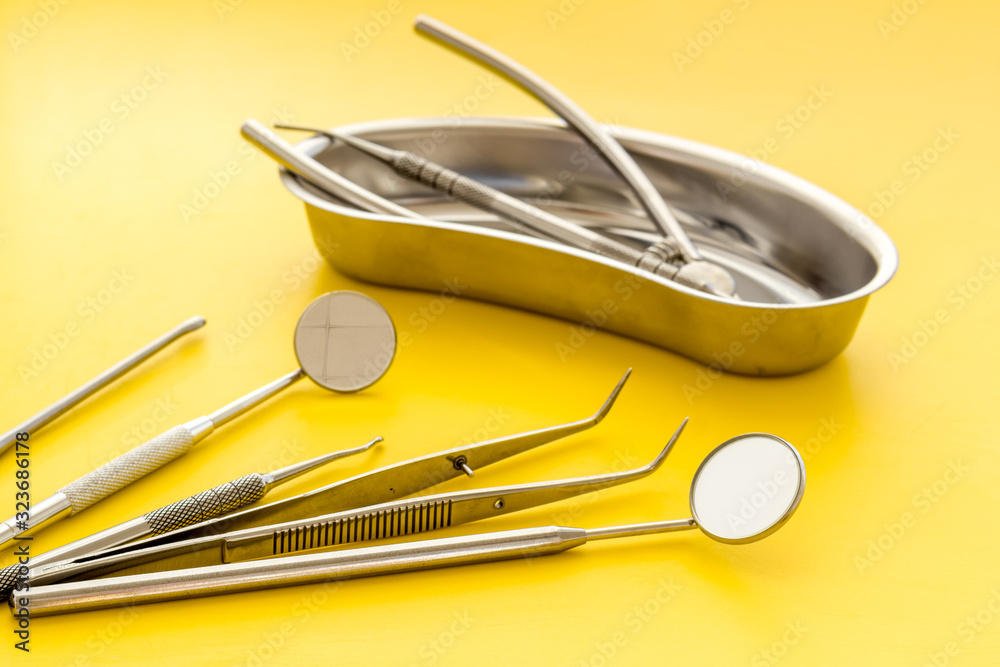 Dental instruments in stainless steel tray on yellow background close up