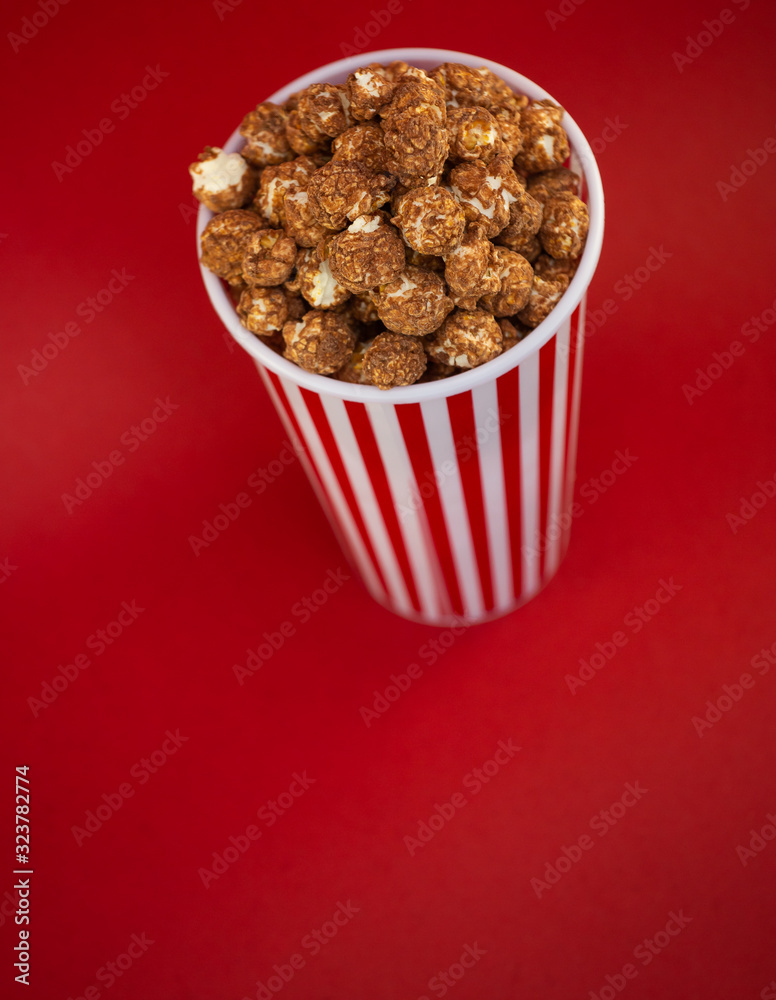 Butter popcorn in a red popcorn cup, snack in the house or cinema on a red background