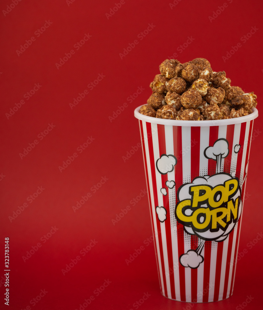 Butter popcorn in a red popcorn cup, snack in the house or cinema on a red background