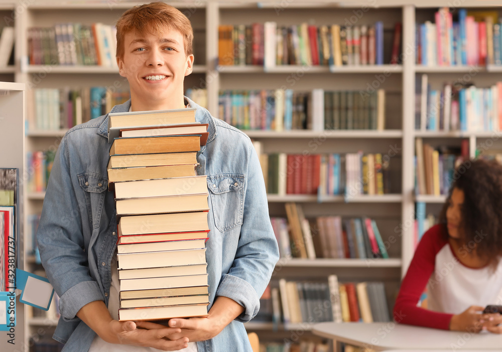 图书馆里拿着一大摞书的男学生画像