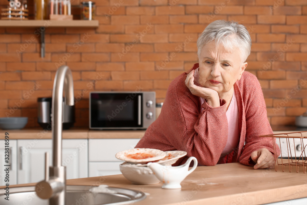 Senior woman with dirty dishes in kitchen