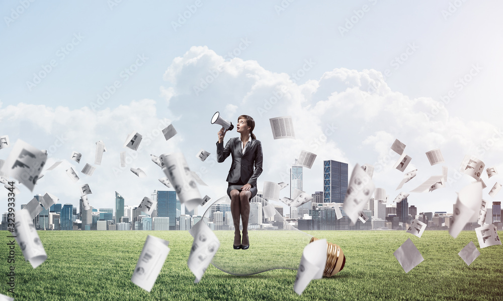 Young woman with megaphone sitting on lightbulb