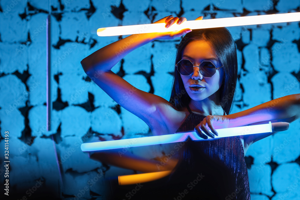 Toned portrait of beautiful woman with neon lamps on dark color background