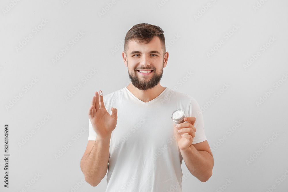 Handsome young man with jar of cream on white background