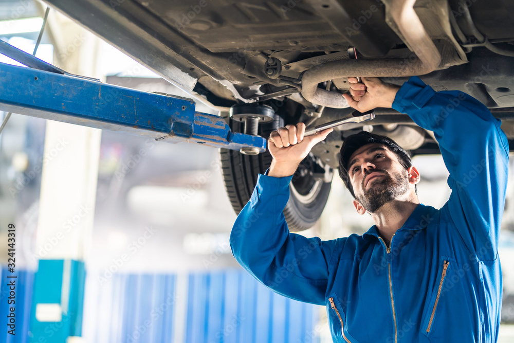 Vehicle service maintenance handsome mens checking under car condition on lifter hoist in garage. Au