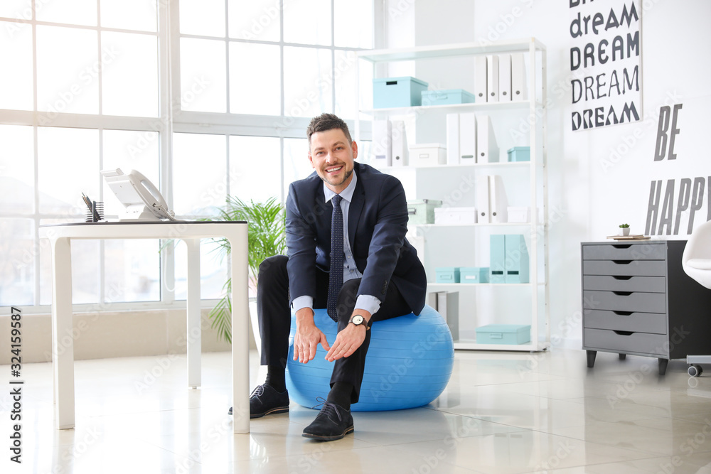 Businessman sitting on fitness ball while working in office