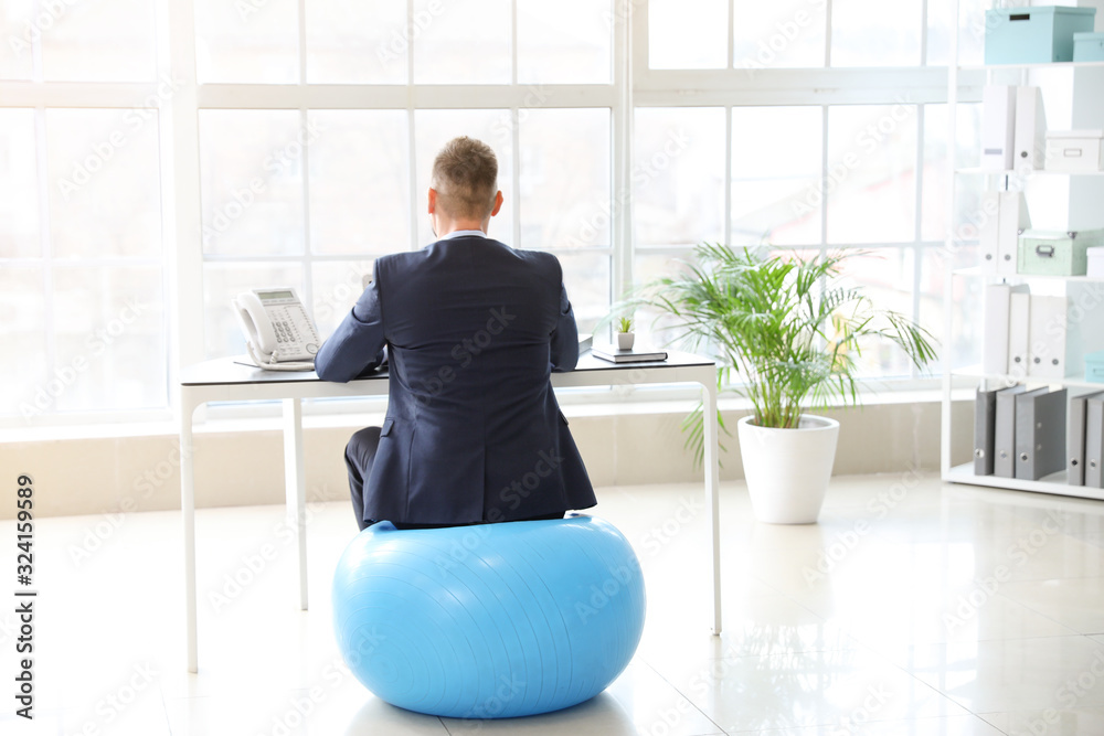 Businessman sitting on fitness ball while working in office