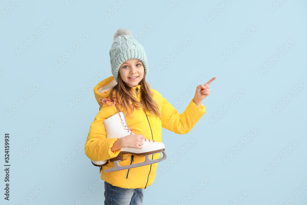 Cute little girl with ice skates showing something on color background