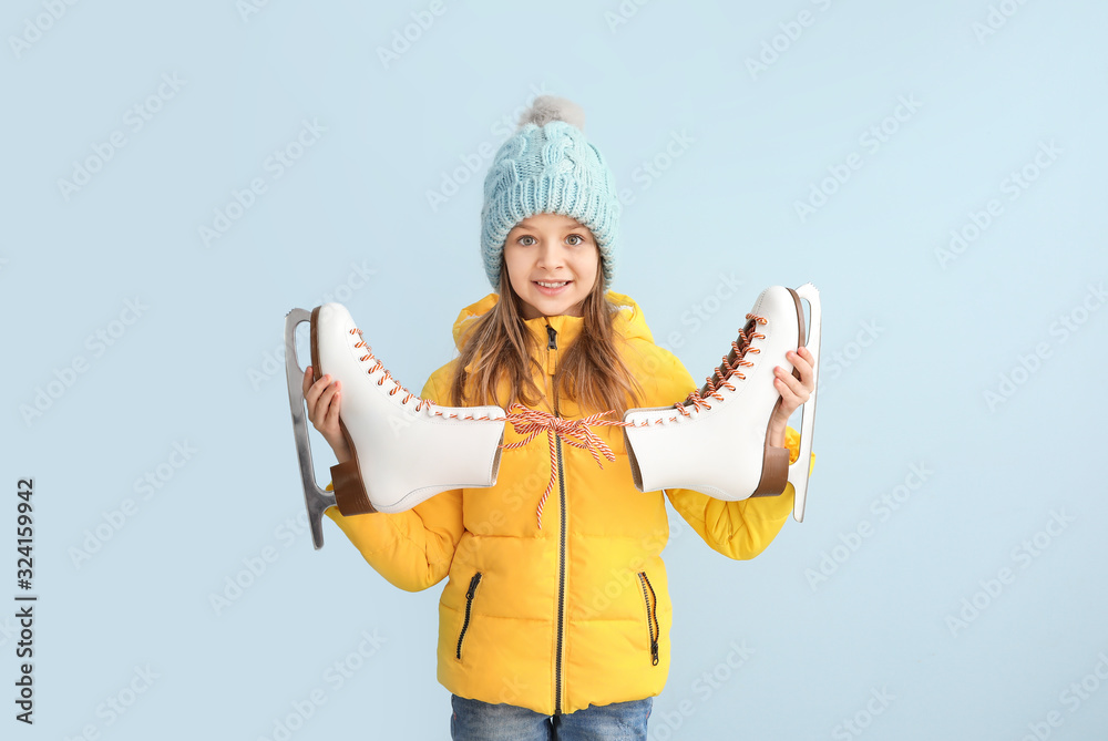 Cute little girl with ice skates on light background