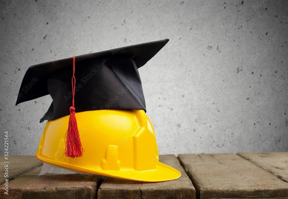 Yellow helmet with graduation hat on the brick table