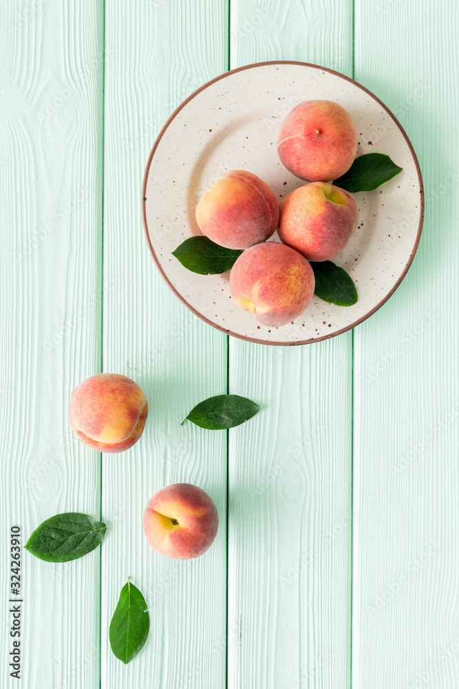 Red peaches pattern with plate and leaves on green wooden table top-down