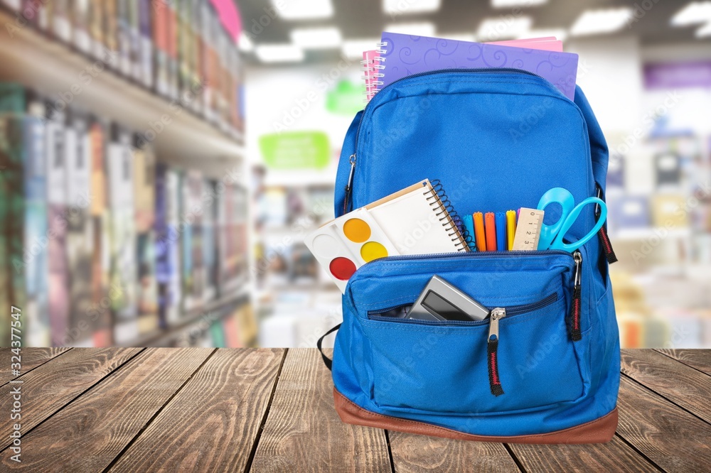 Classic school backpack with colorful school supplies and books on desk.