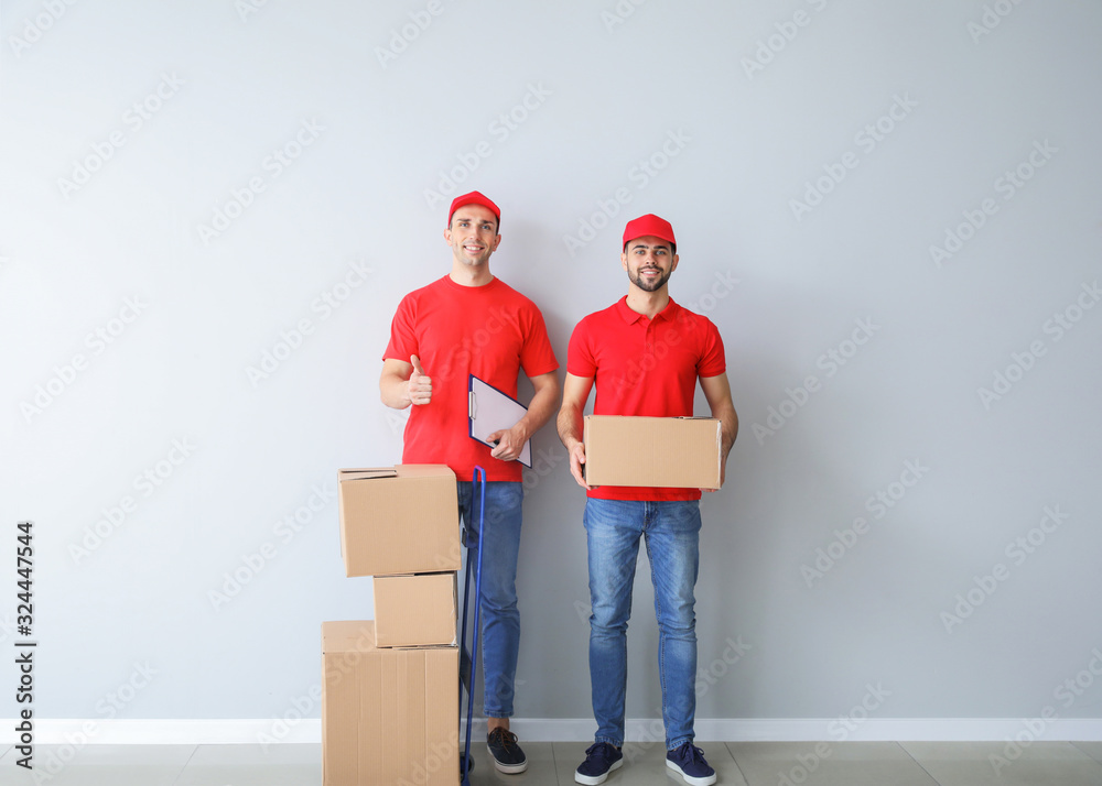 Delivery men with boxes near light wall