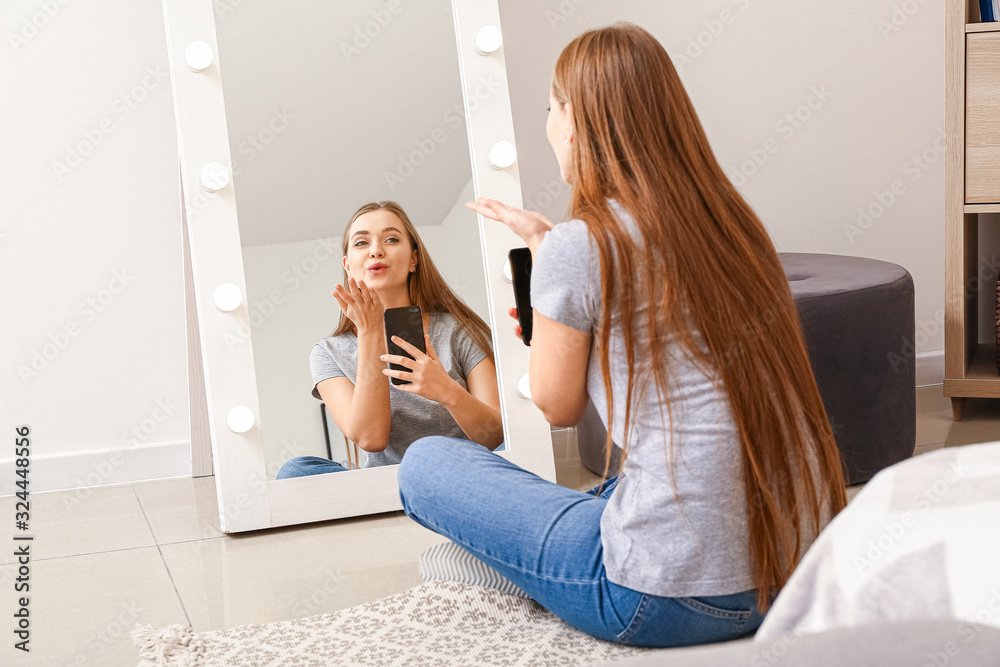 Beautiful young woman taking selfie in front of mirror at home