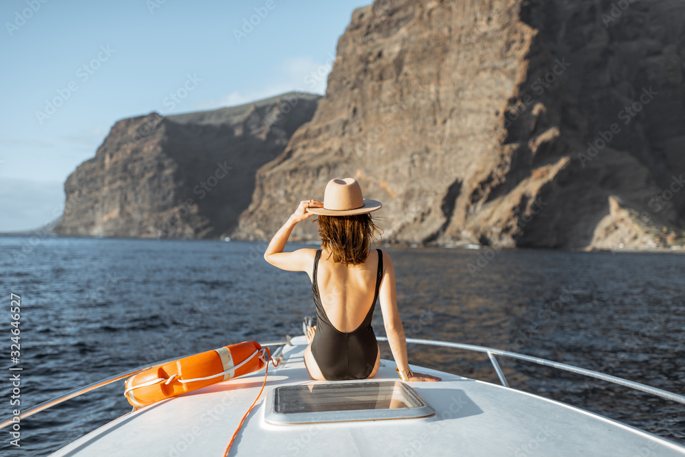 Woman enjoying ocean voyage sitting with lifebuoy on the yacht nose while sailing near the breathtak