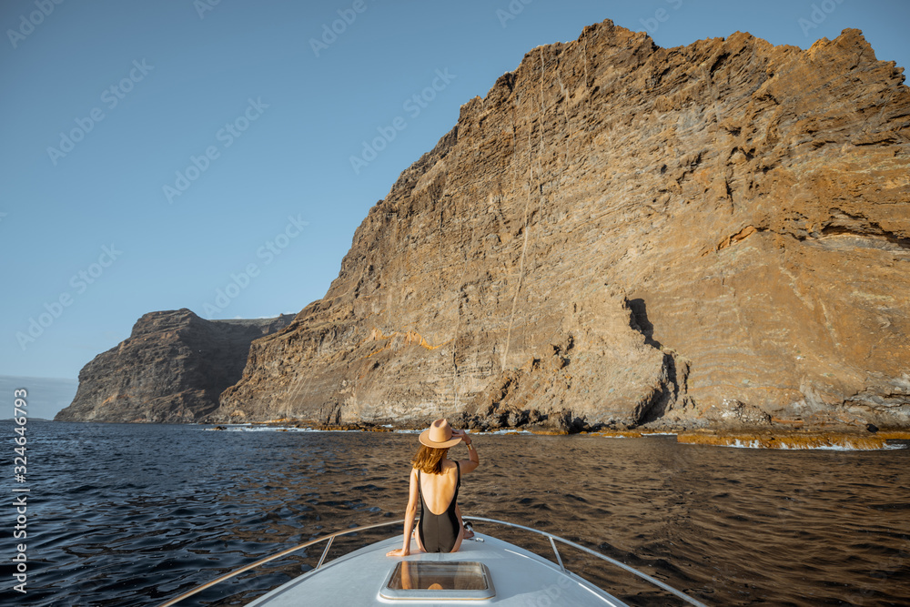 Woman in swimsuit and sun hat enjoying ocean voyage sitting on the yacht nose while sailing near the