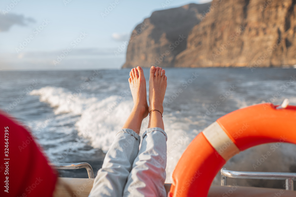 Young woman with lifebuoy enjoying sea voyage, sailing on a yacht near a rocky shore. Concept of a c