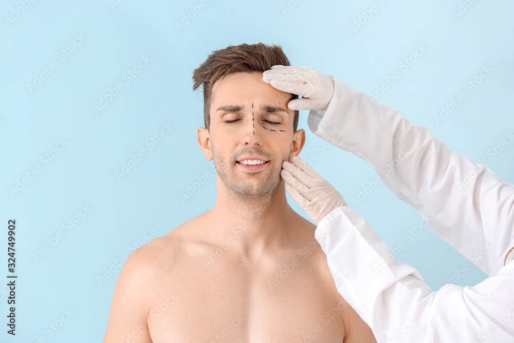 Plastic surgeon touching face of young man on color background