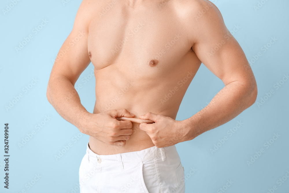 Young man touching his belly fat on color background. Plastic surgery concept