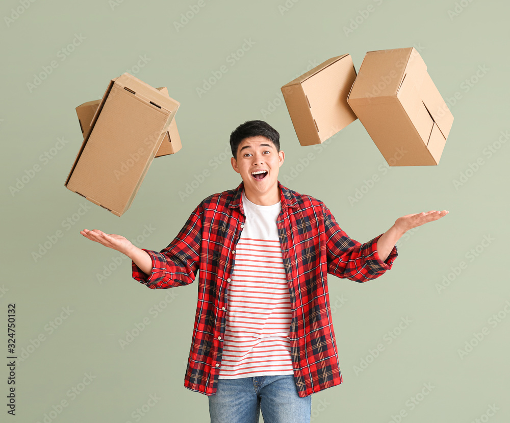 Asian man with moving boxes on color background