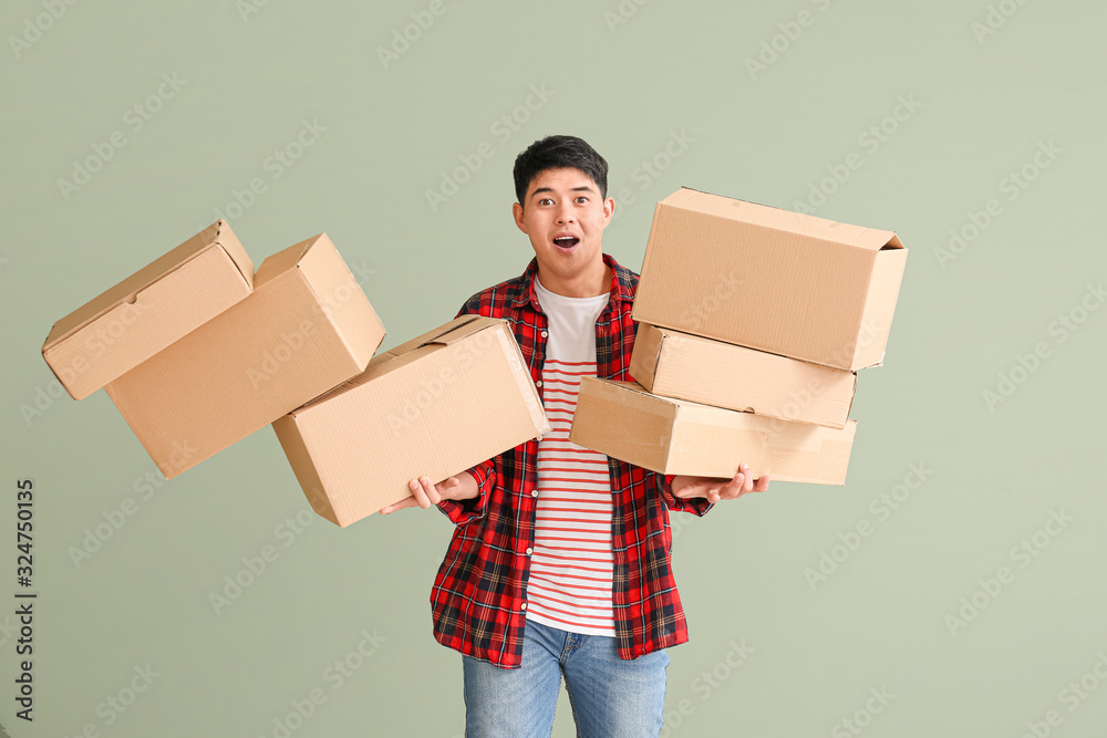 Asian man dropping moving boxes on color background