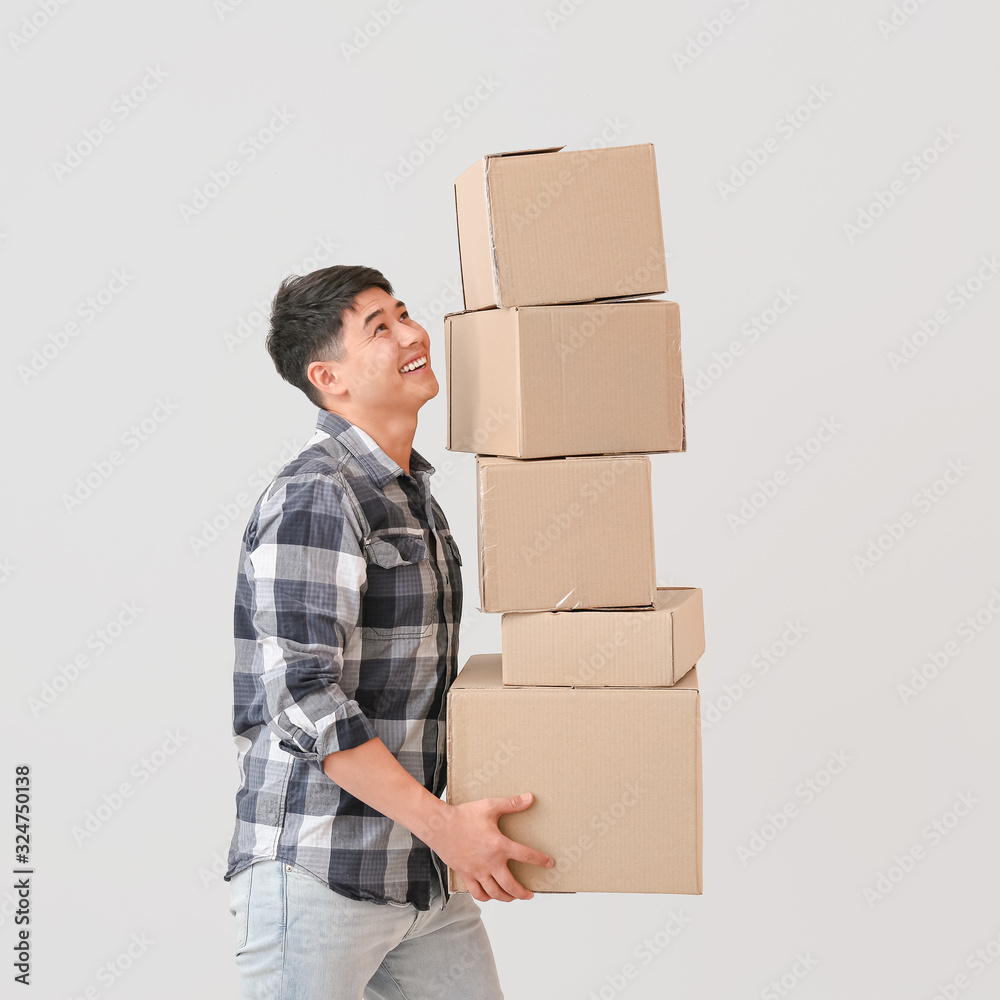 Asian man with moving boxes on light background