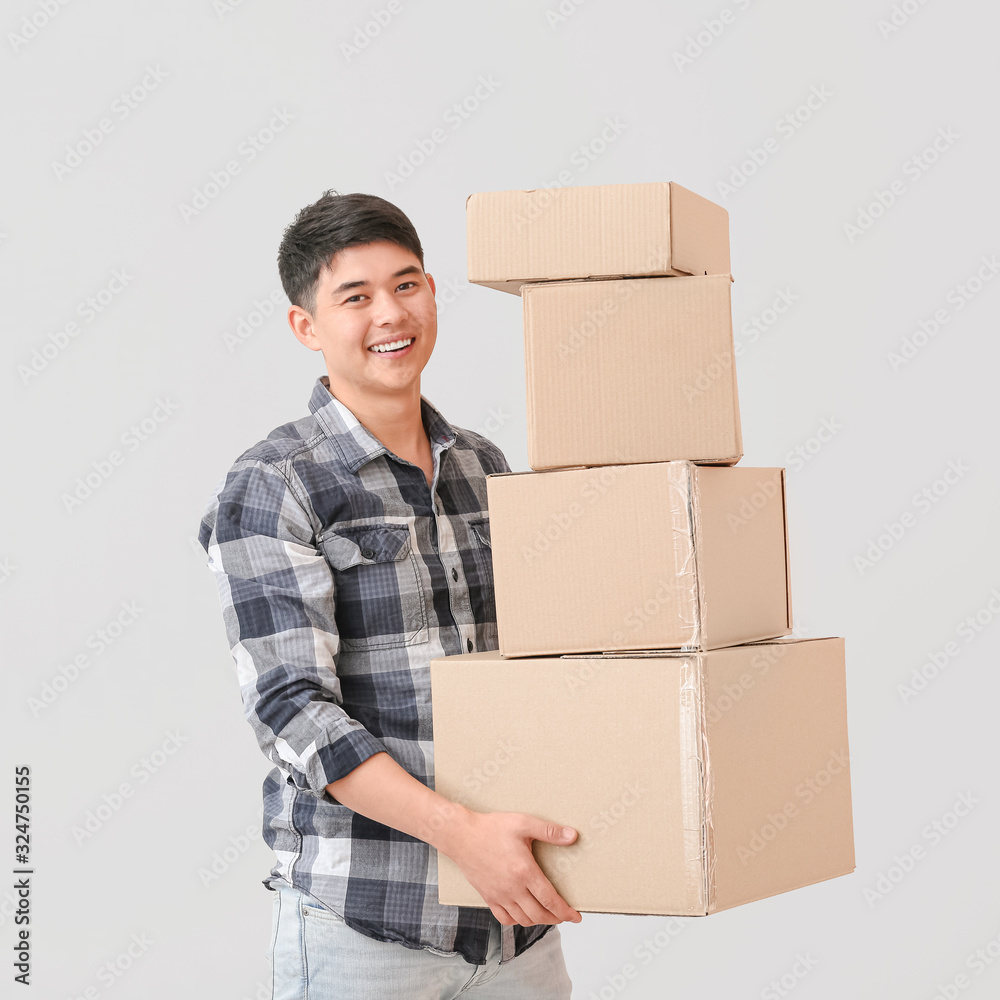 Asian man with moving boxes on light background